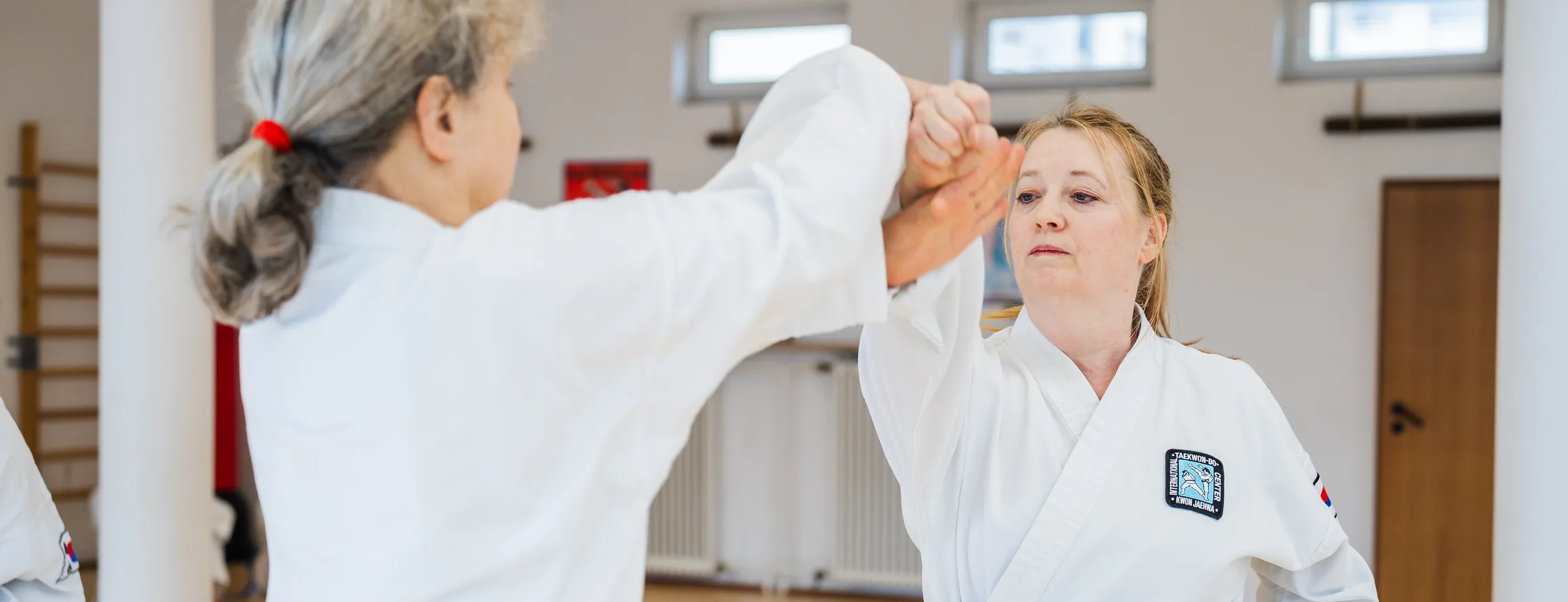 Zwei Frauen mit schwarzem Gürtel in einer Selbstverteidigungsübung: eine fängt den Faustangriff der anderen ab und kontrolliert deren Arm