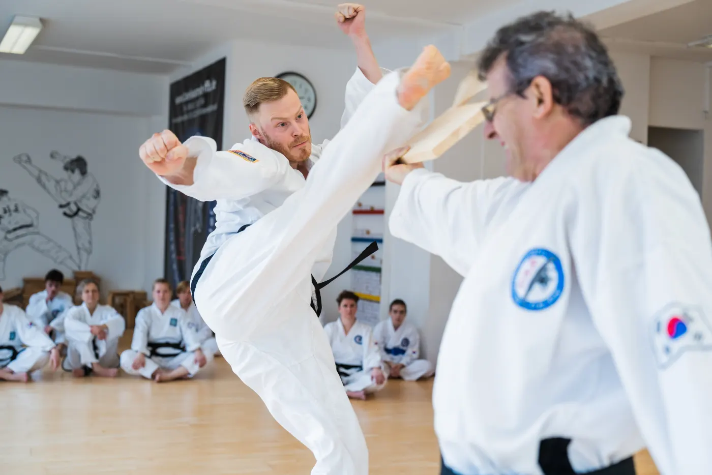Mann im Taekwon-Do-Anzug durchschlägt ein Holzbrett mit einem Fußtritt