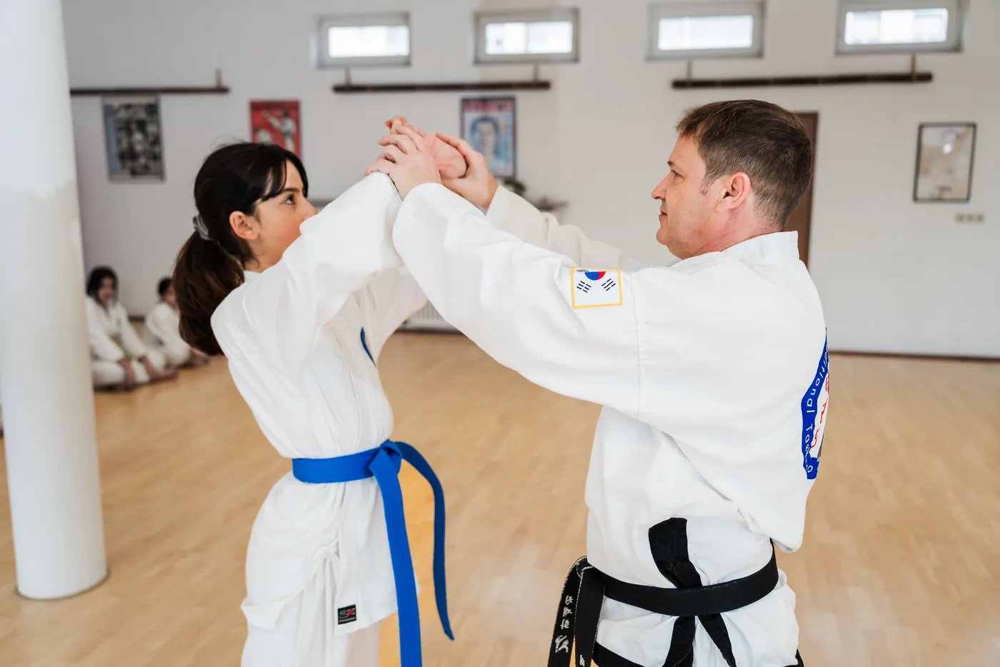 Mädchen im Taekwon-Do-Anzug blockt den Arm des Trainers bei einer Selbstverteidigungsübung