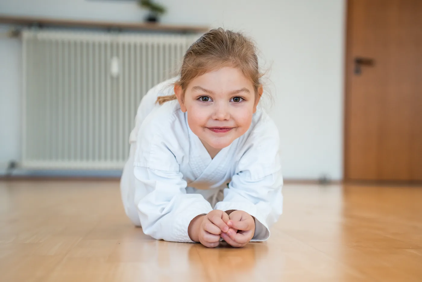 Kleines Mädchen im Taekwon-Do-Anzug liegt auf dem Hallenboden und lächelt in die Kamera